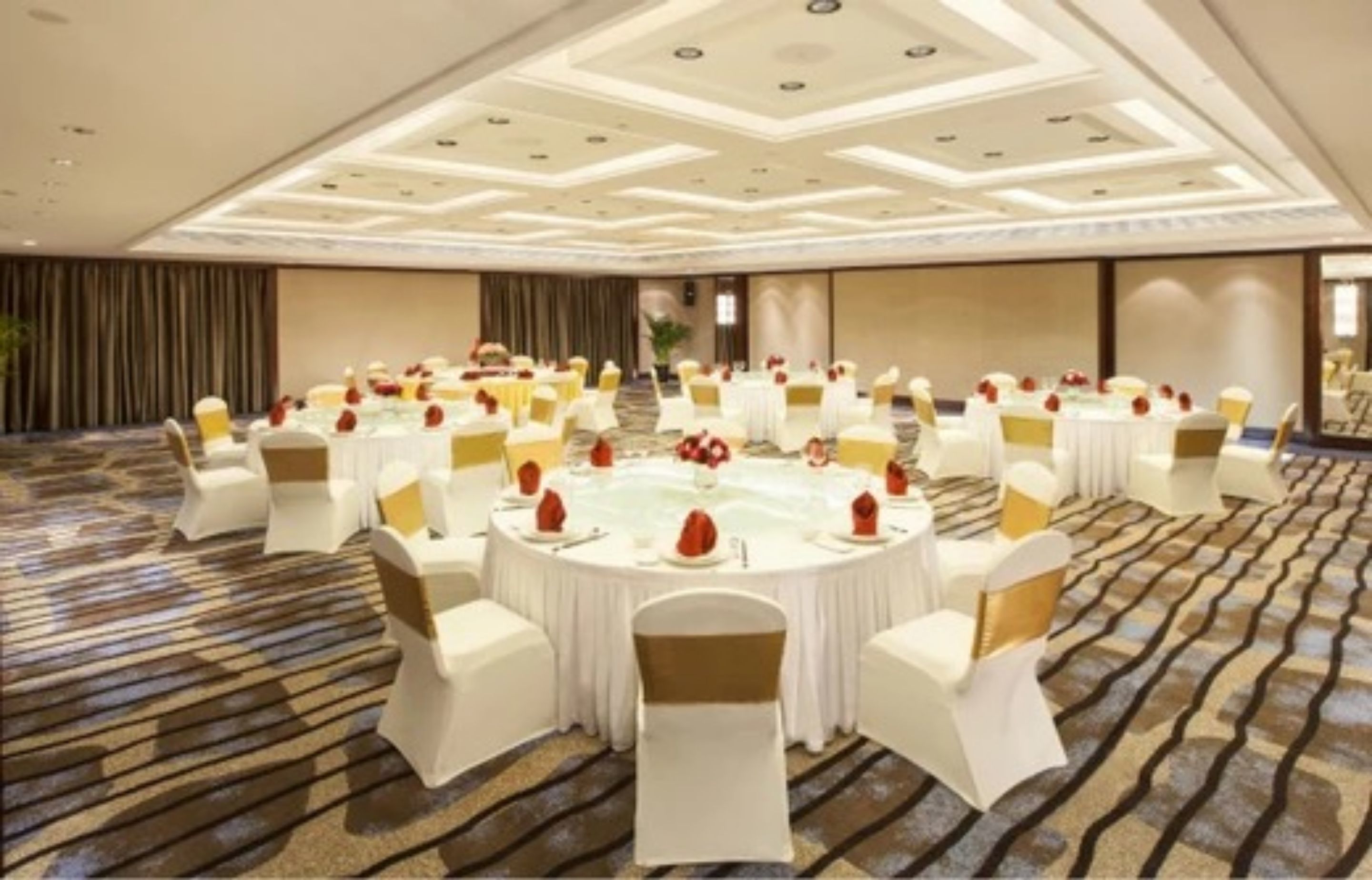 Un amplio salón de conferencias con mesas redondas, sillas blancas y centros de mesa rojos.