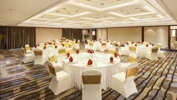 Un amplio salón de conferencias con mesas redondas, sillas blancas y centros de mesa rojos.