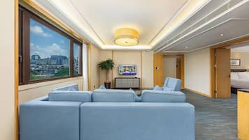 A hotel room with a large window, a seating area, a television, and a city view.