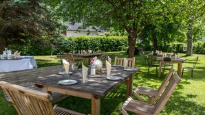 An outdoor dining area with wooden tables and chairs, surrounded by lush greenery and trees.