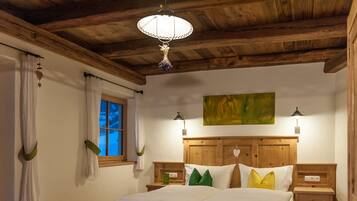 Ein Schlafzimmer mit Holzboden, einem Bett mit weißer Bettwäsche, grün-gelben Kissen, zwei Nachttischen und einem Fenster mit Vorhängen.