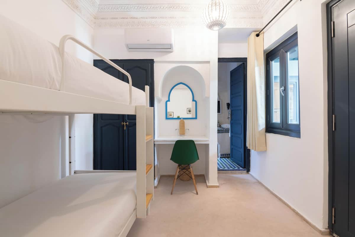 Una habitación con literas, un escritorio con silla, un espejo y una ventana.