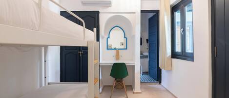 A room with bunk beds, a desk with a chair, a mirror, and a window.