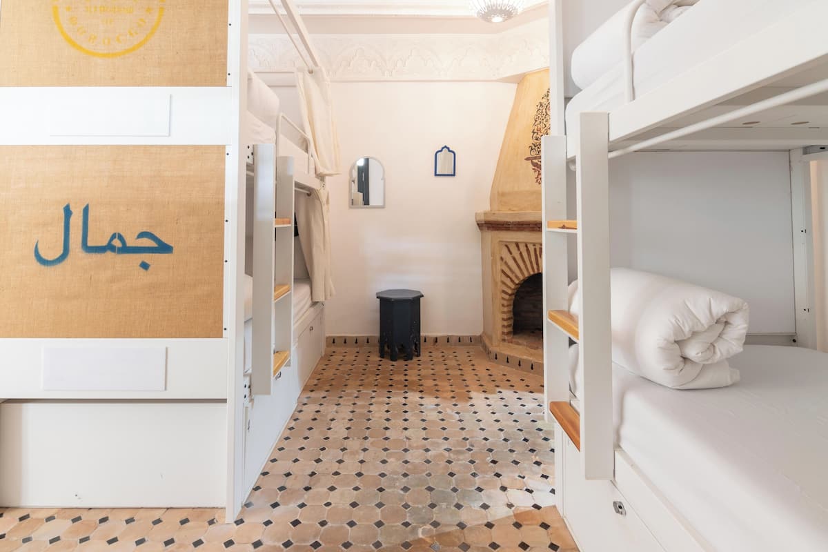 Habitación pequeña y bien iluminada, con suelo de baldosas, camas literas, un espejo y una chimenea.
