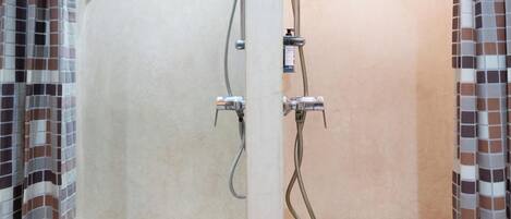 Doccia con pavimento a scacchi e pareti piastrellate, dotata di soffione e doccetta.