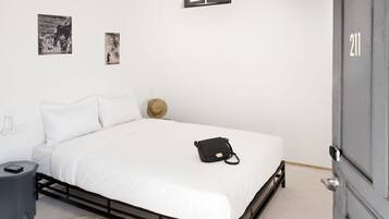 A neatly made bed with white bedding, a black bag on the bed, a small bedside table, and a wall-mounted picture.