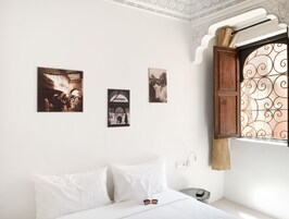 Un dormitorio con una cama, almohadas blancas, una mesita de noche, una lámpara de pared y tres cuadros enmarcados.