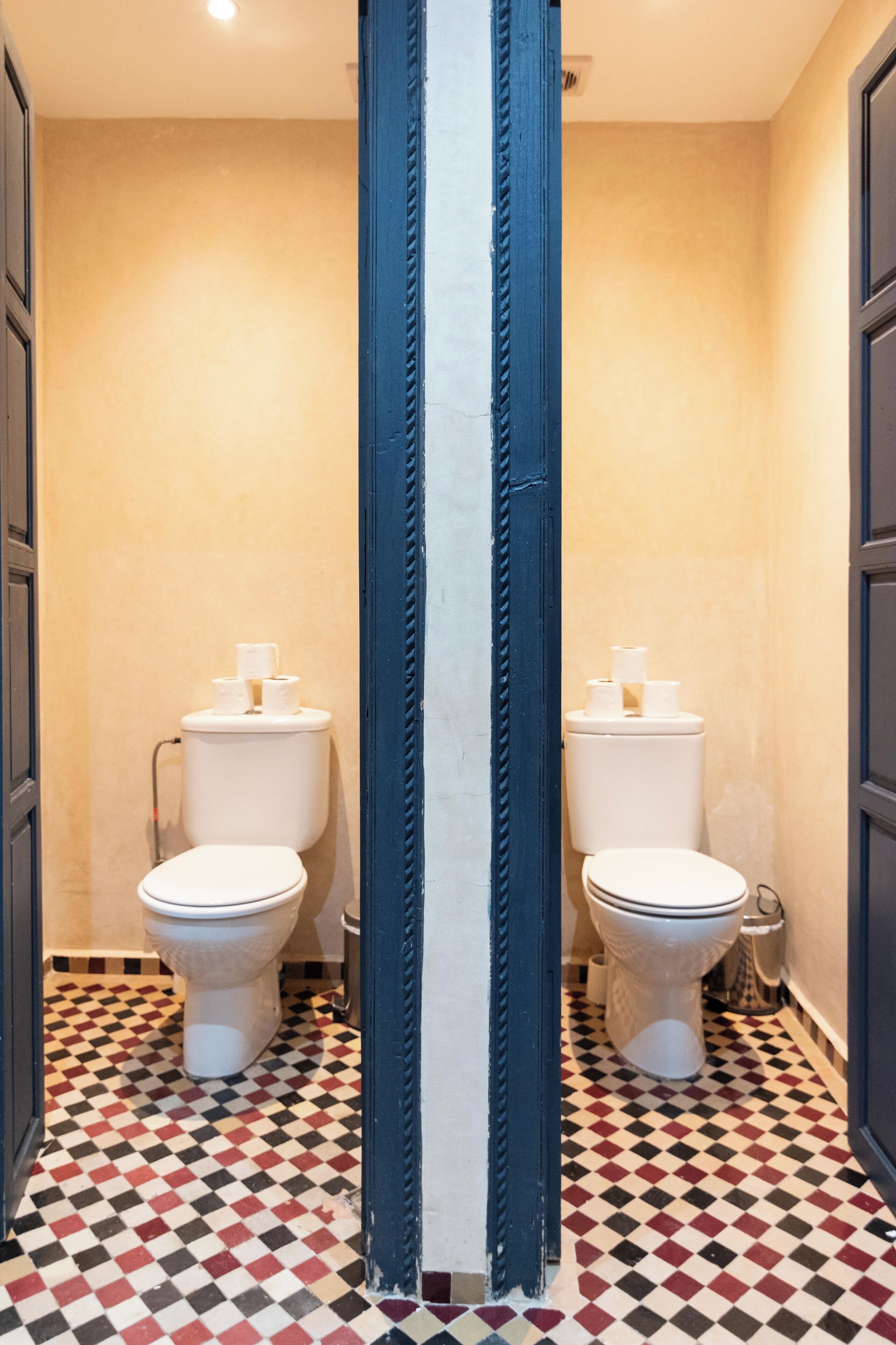 A bathroom with two toilets, a checkered floor, and a blue door frame.