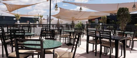 Un espace extérieur aménagé en terrasse, avec des tables et des chaises rondes, protégé par de grands parasols et agrémenté de luminaires suspendus de style lanterne.