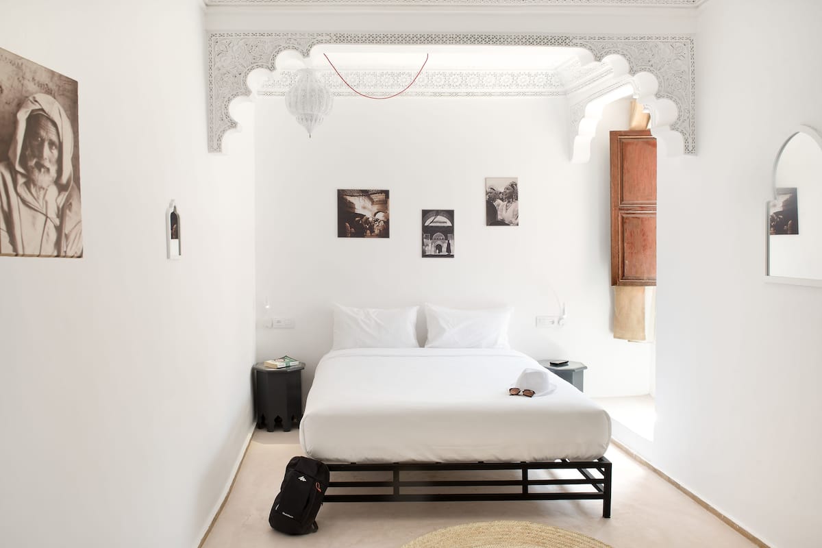 Un dormitorio minimalista con cama, mesita de noche, maleta y cuadros en la pared.