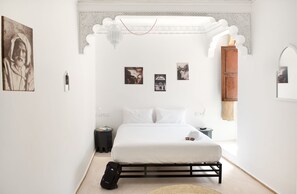 A minimalist bedroom with a bed, a nightstand, a suitcase, and wall art.