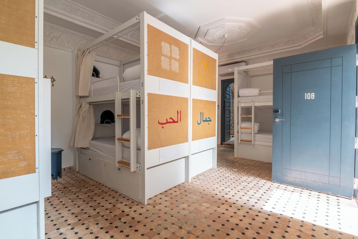 Habitación de hotel con literas, una puerta azul con la etiqueta '108' y un suelo estampado.