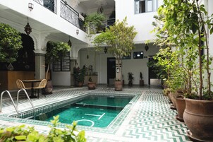 A swimming pool with a geometric tile pattern, surrounded by potted plants and a seating area with wicker chairs.