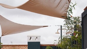 Un espacio exterior iluminado por el sol con cojines color beige, una planta en maceta y una lámpara fijada a la pared.
