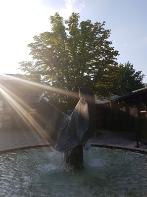 Une sculpture de cheval dans une fontaine, avec les rayons du soleil filtrant à travers les arbres.