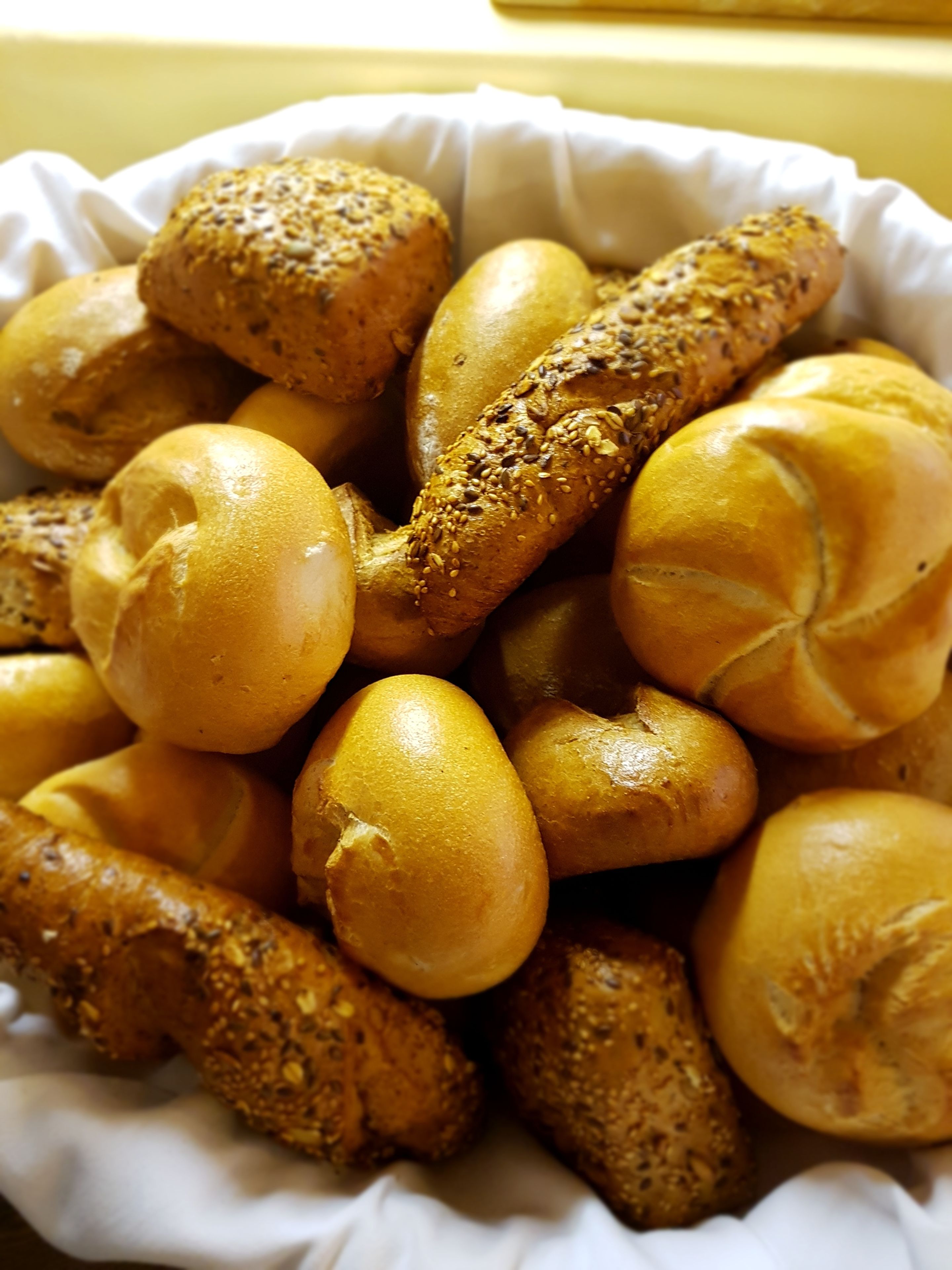 Eine Schüssel mit verschiedenen Brötchen, manche mit Saaten, auf einer weißen Papierunterlage.