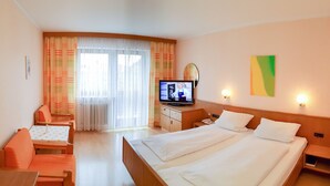 A hotel room with two beds, a desk, a chair, a television, and a window with curtains. - Kurhotel Anders (Bad Fuessing)