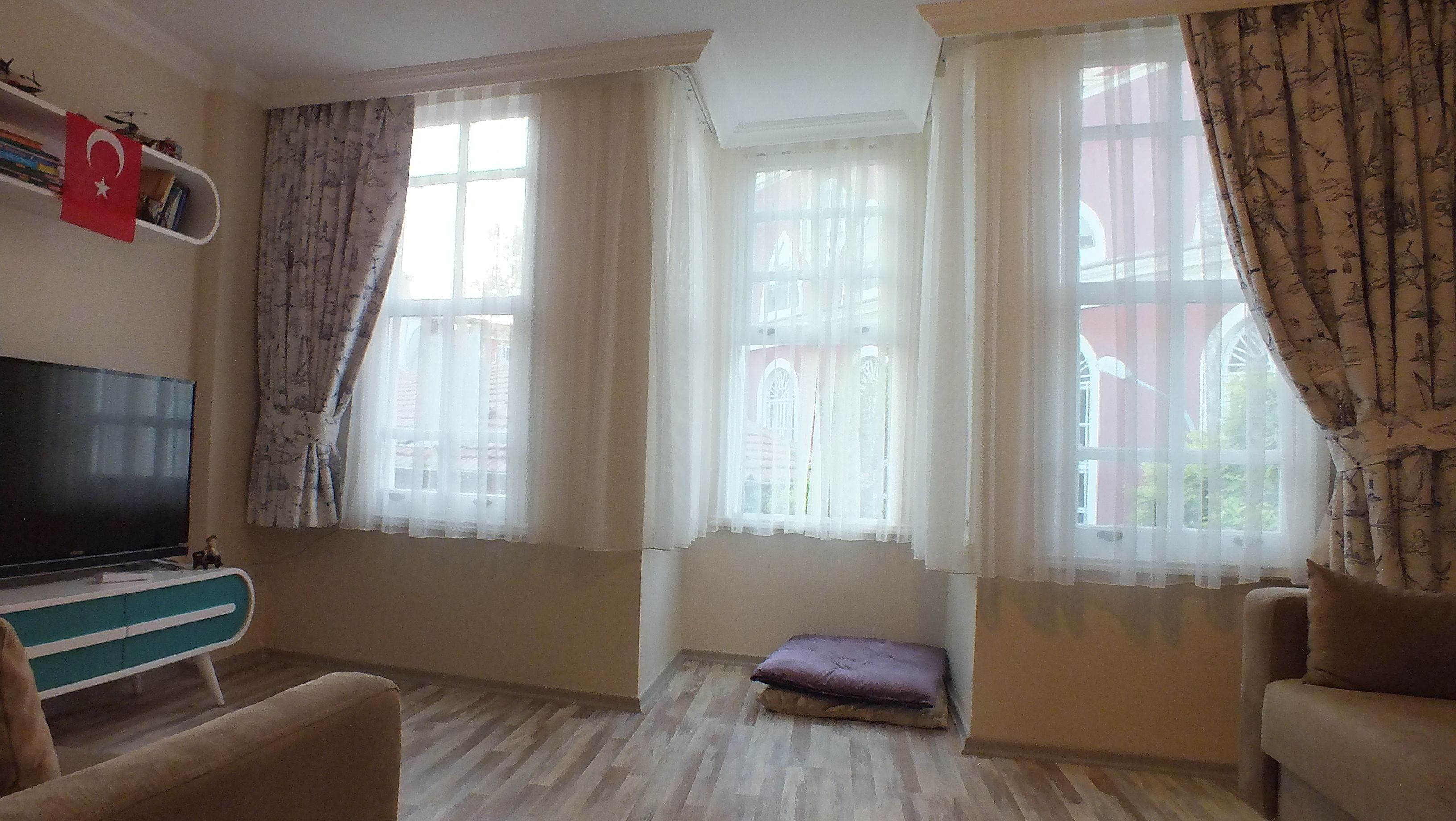 A living room with a television, a sofa, a small table, and a window with curtains.