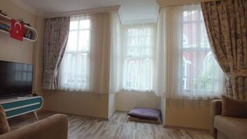A living room with a television, a sofa, a small table, and a window with curtains.