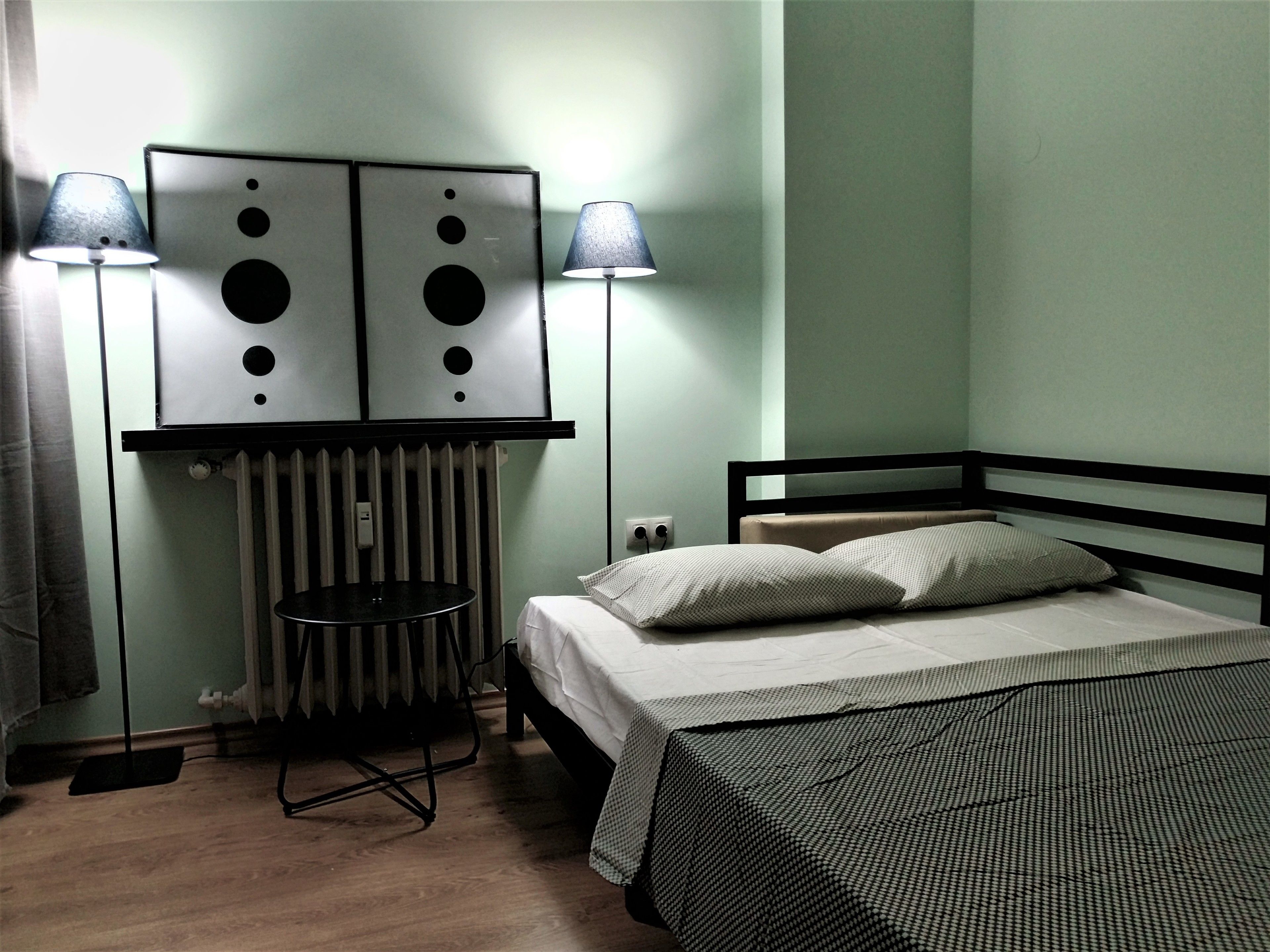 A bedroom with a bed, two wall-mounted lamps, a radiator, and a small table.