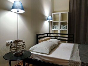 Un dormitorio ordenado con cama, lámparas de noche, una mesita y una ventana con cortinas.