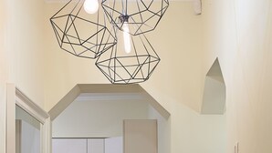 Un pasillo estrecho que conduce a una cocina con armarios blancos, salpicadero de azulejos y una lámpara colgante.