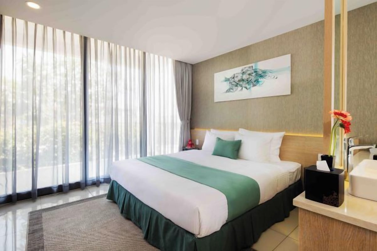 A hotel room with a large bed, a bedside table, a mirror, and a window with curtains.