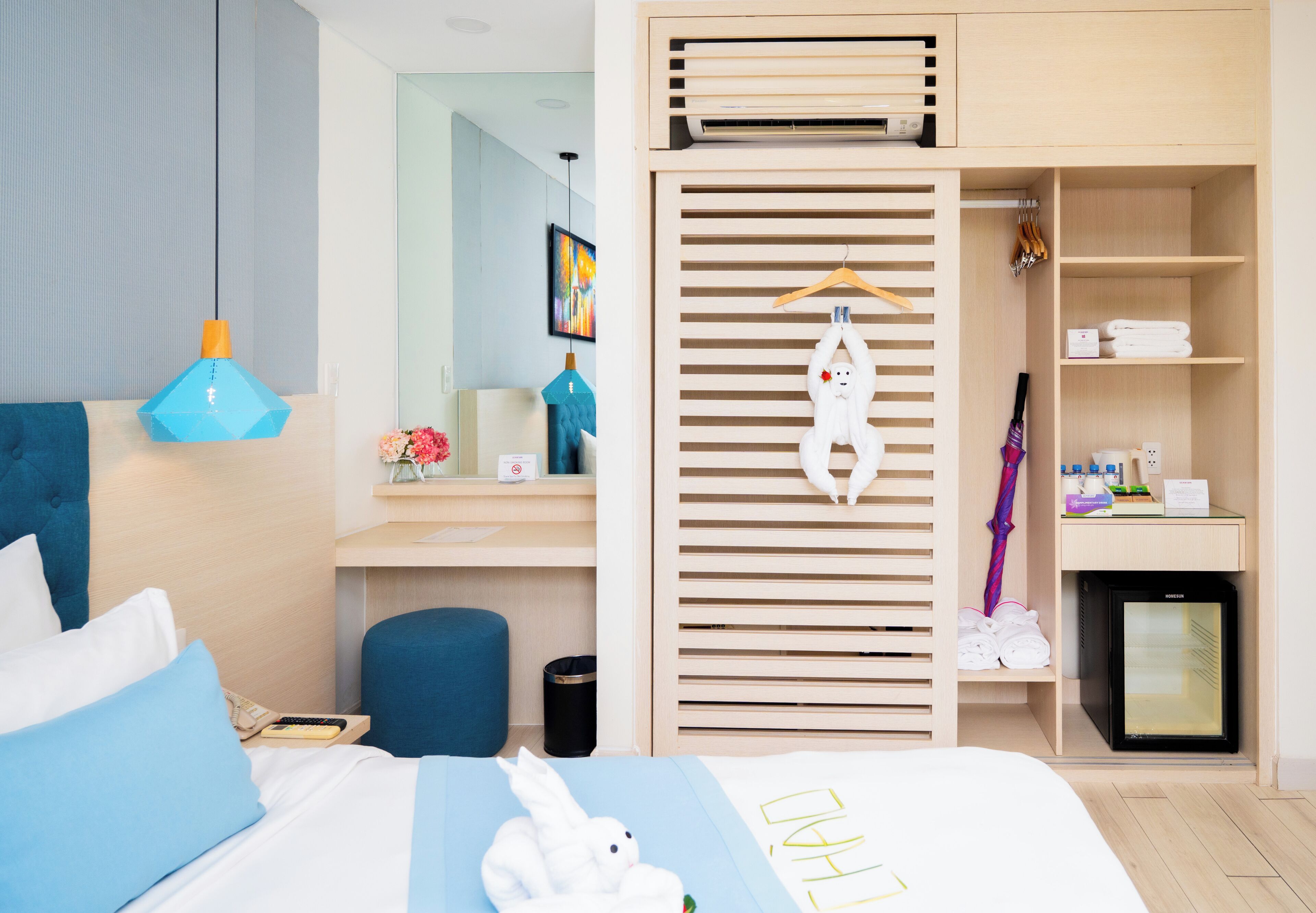 Quarto de hotel moderno com cama, escrivaninha, guarda-roupa e mini-geladeira.