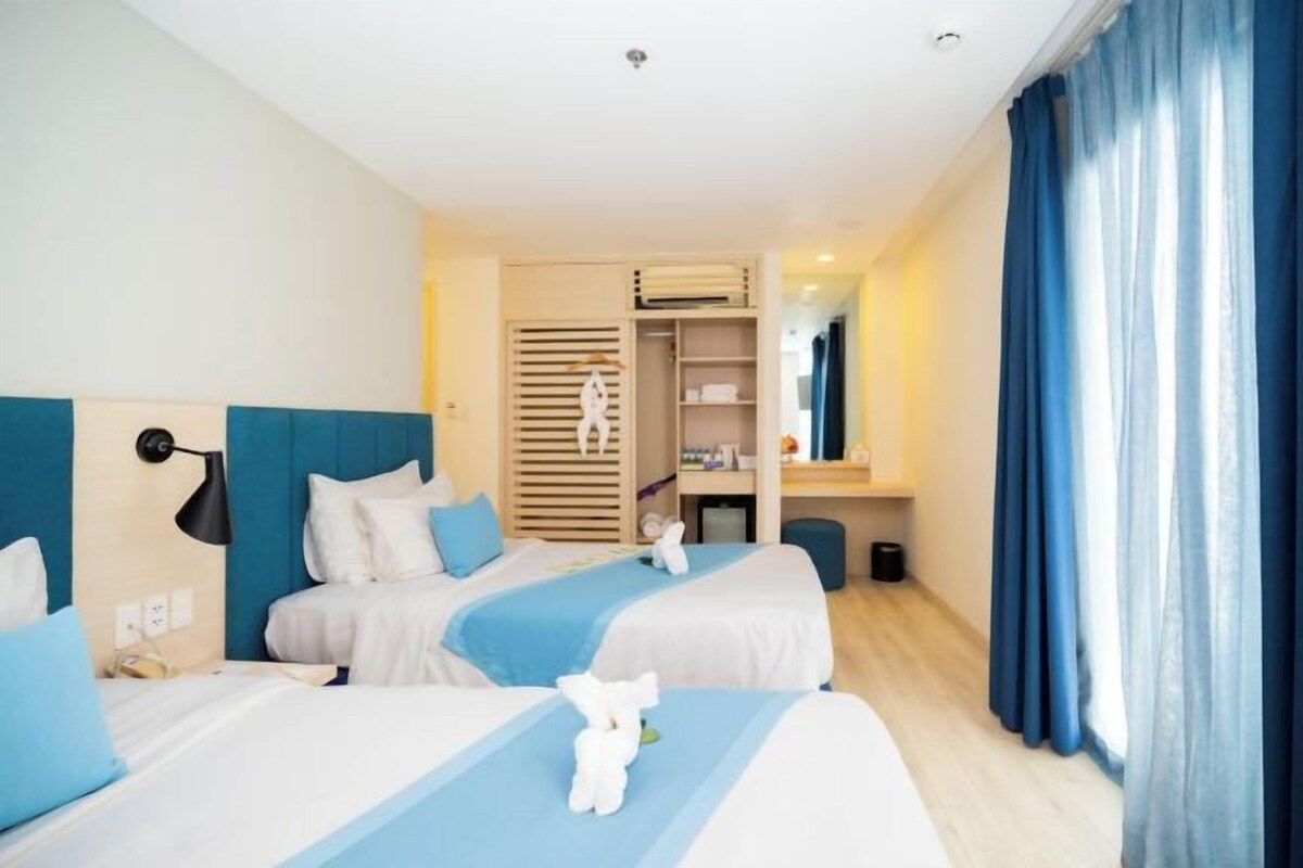 A hotel room with two beds, a wardrobe, a mirror, and a window with curtains.
