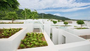 Un jardín moderno en la azotea con macetas blancas y plantas verdes, rodeado de un cielo despejado y montañas distantes.