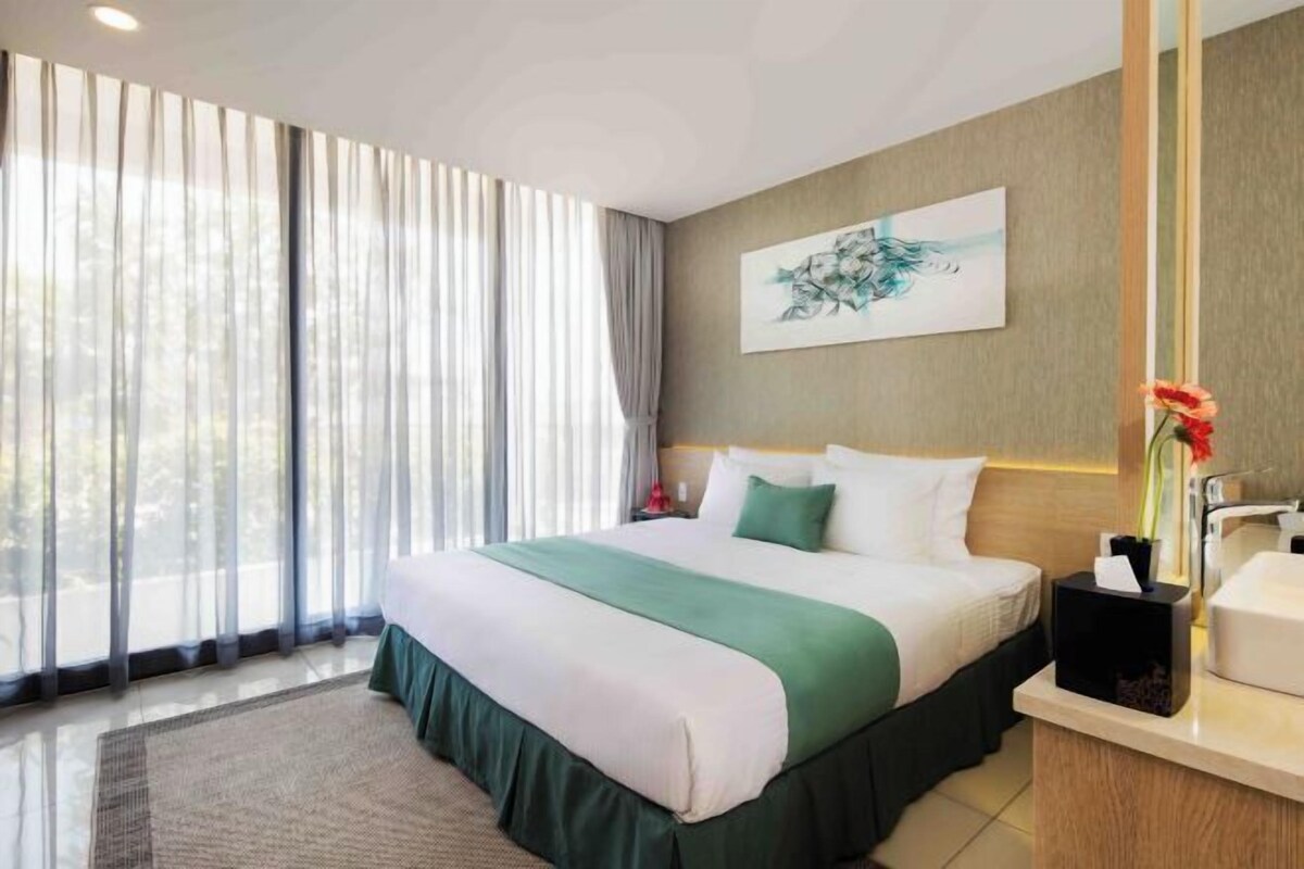 Una habitación de hotel con una cama grande, una mesita de noche con un jarrón de flores, un cuadro en la pared y vistas por la ventana.