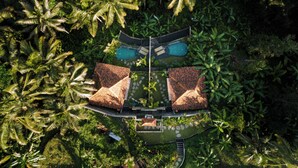 Vista aérea de un resort con dos piscinas separadas, un camino central y un pequeño jardín.