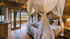 Una habitación con cama bajo un dosel, pisos de madera, un escritorio pequeño y vista a través de un ventanal.