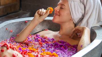 A person in a bathtub filled with colorful flower petals.