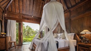 Habitación de madera con cama bajo dosel, mesita de noche y vista a zonas verdes al exterior.