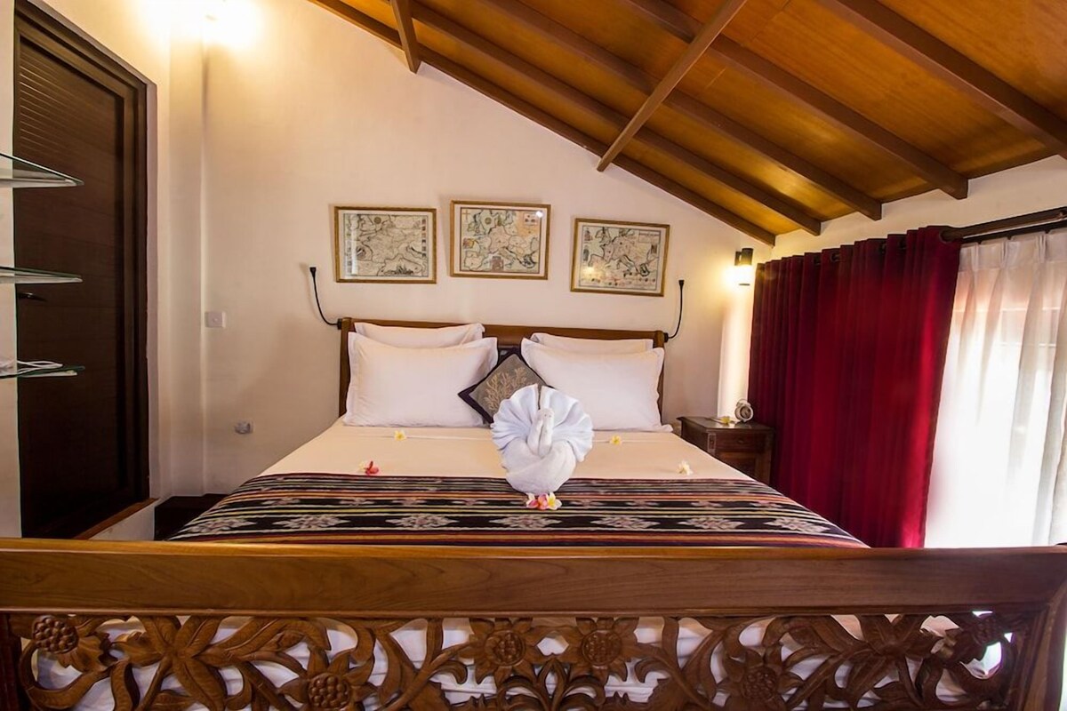 Une chambre d’hôtel avec un lit, une tête de lit en bois et un rideau rouge.