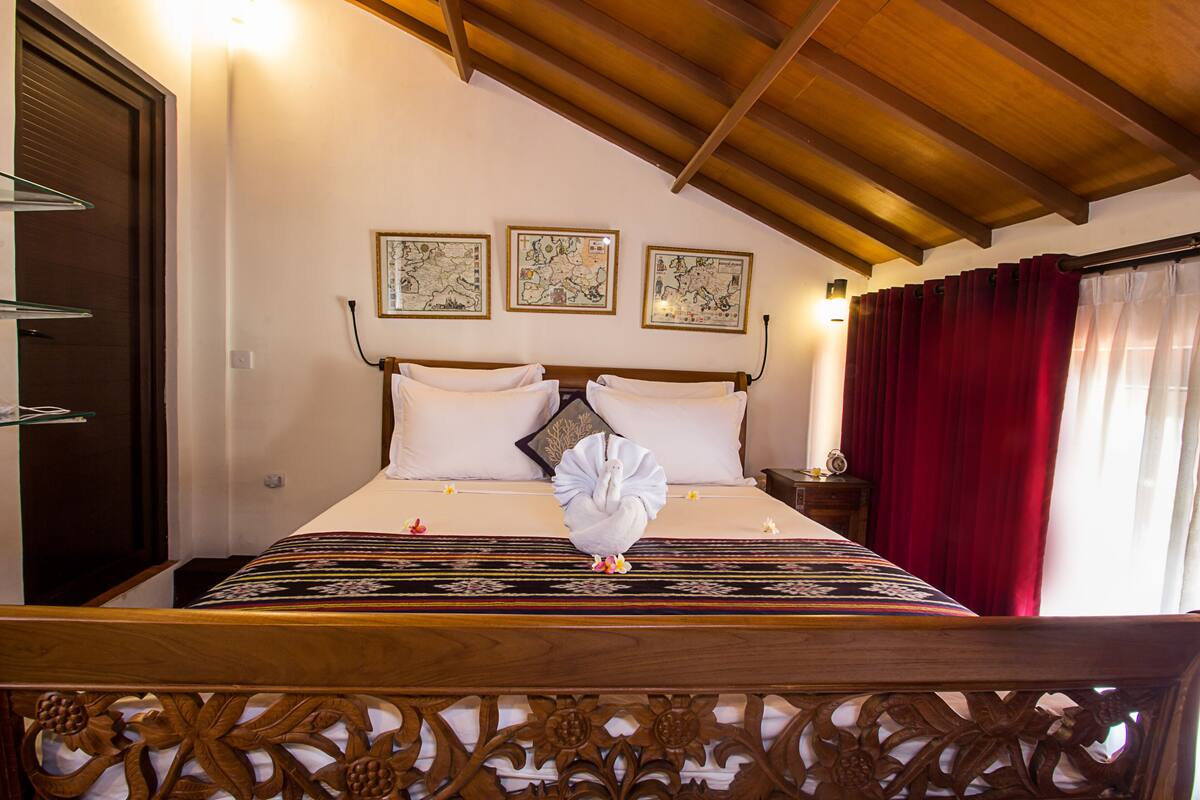 Une chambre d’hôtel avec un lit en bois, un rideau rouge et trois tableaux encadrés accrochés au mur.