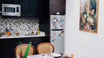 Una cocina con armarios oscuros, microondas, refrigerador con imanes, salpicadero de azulejos y una mesa de comedor con sillas.