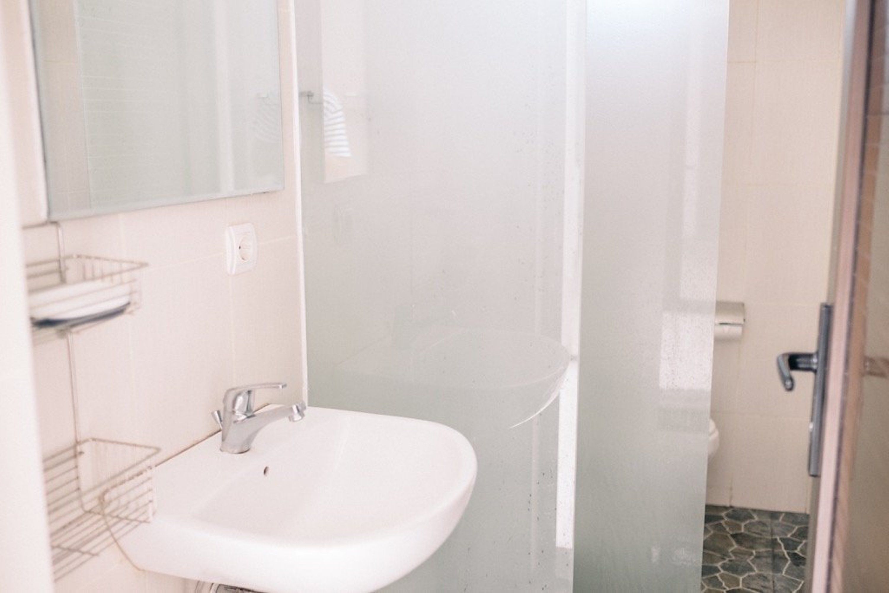 Un baño con lavamanos blanco, un espejo y zona de ducha.