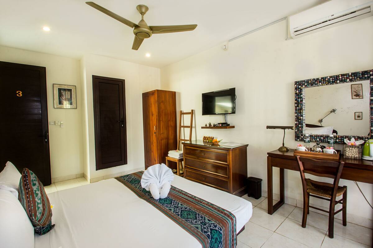 Une chambre d’hôtel équipée d’un lit, d’un bureau, d’une chaise, d’une télévision, d’une armoire et d’un ventilateur de plafond.
