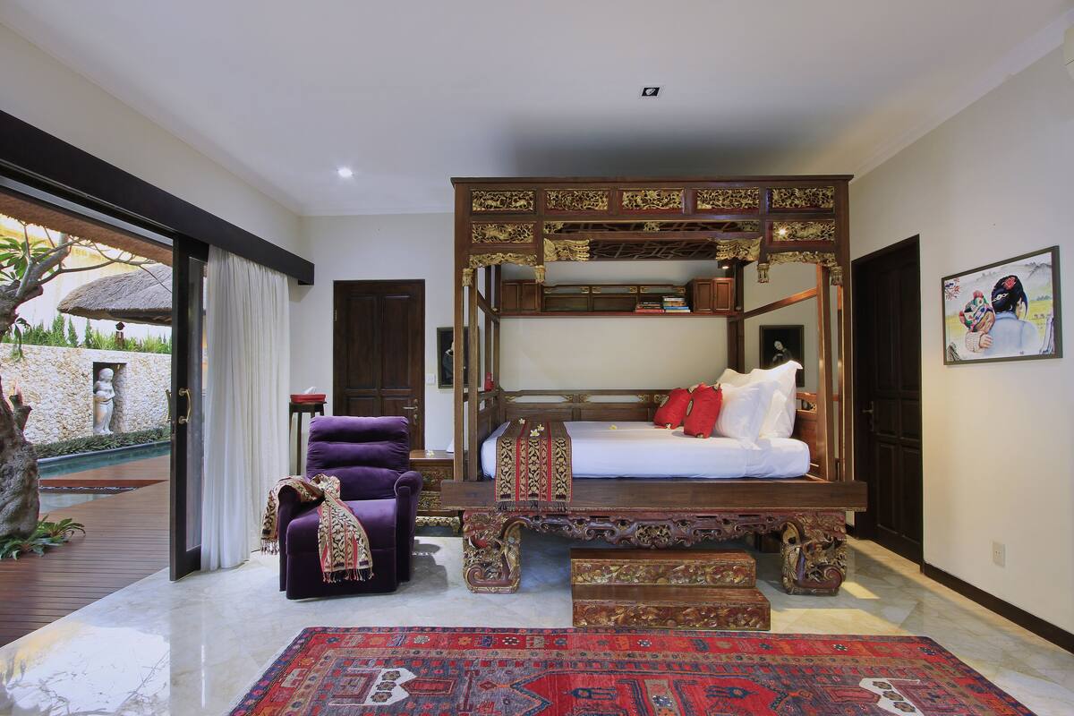 Una camera da letto con un letto a baldacchino, una poltrona viola e un tappeto con motivi neri e rossi.