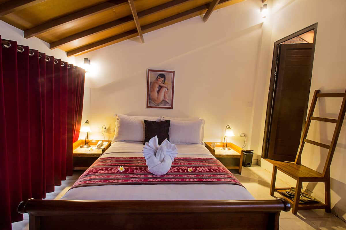 Une chambre d’hôtel avec un lit, un rideau rouge, un tableau au mur et une chaise en bois.