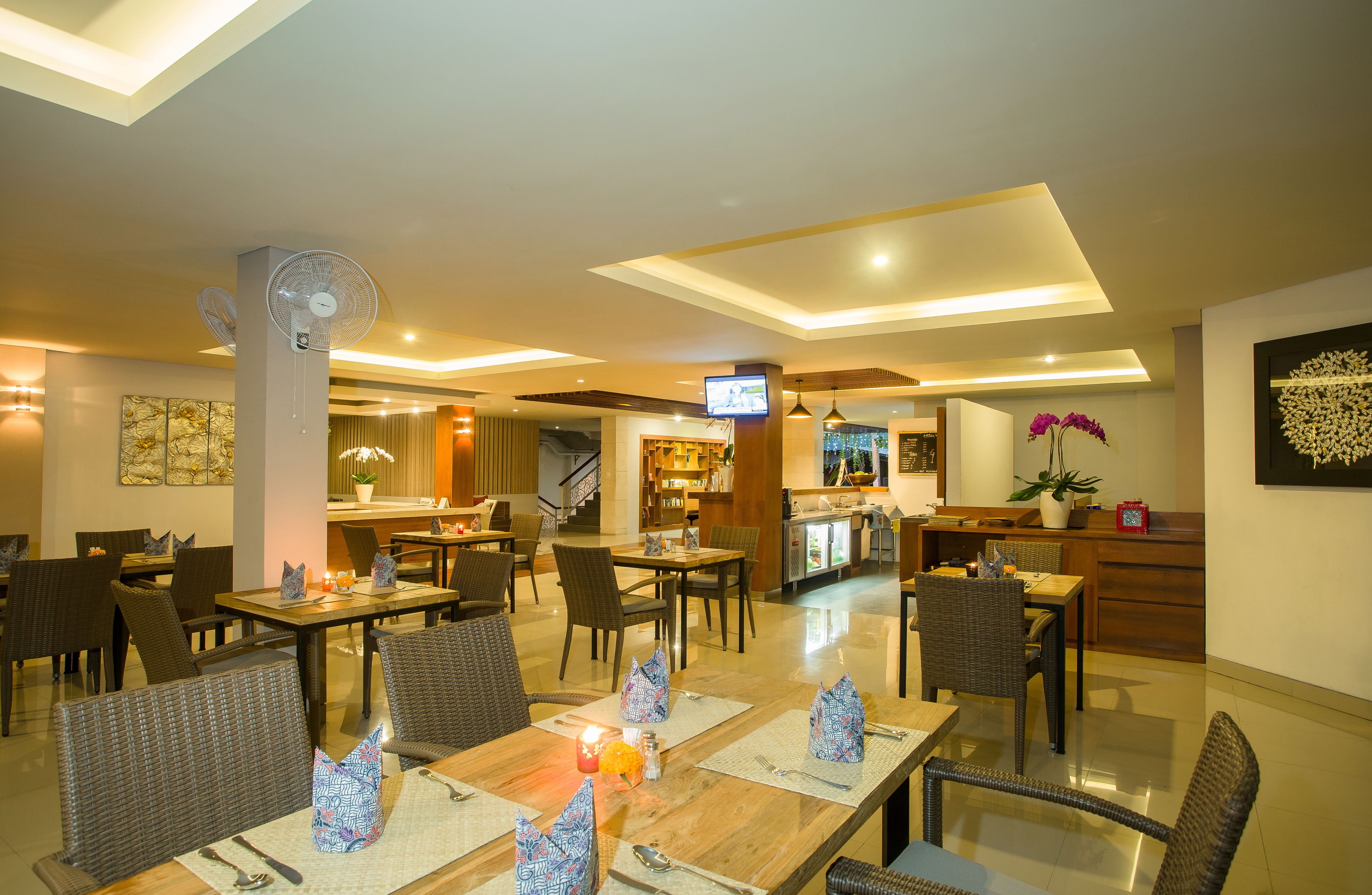 A well-lit restaurant with multiple dining tables and chairs, a bar area, and a television screen.