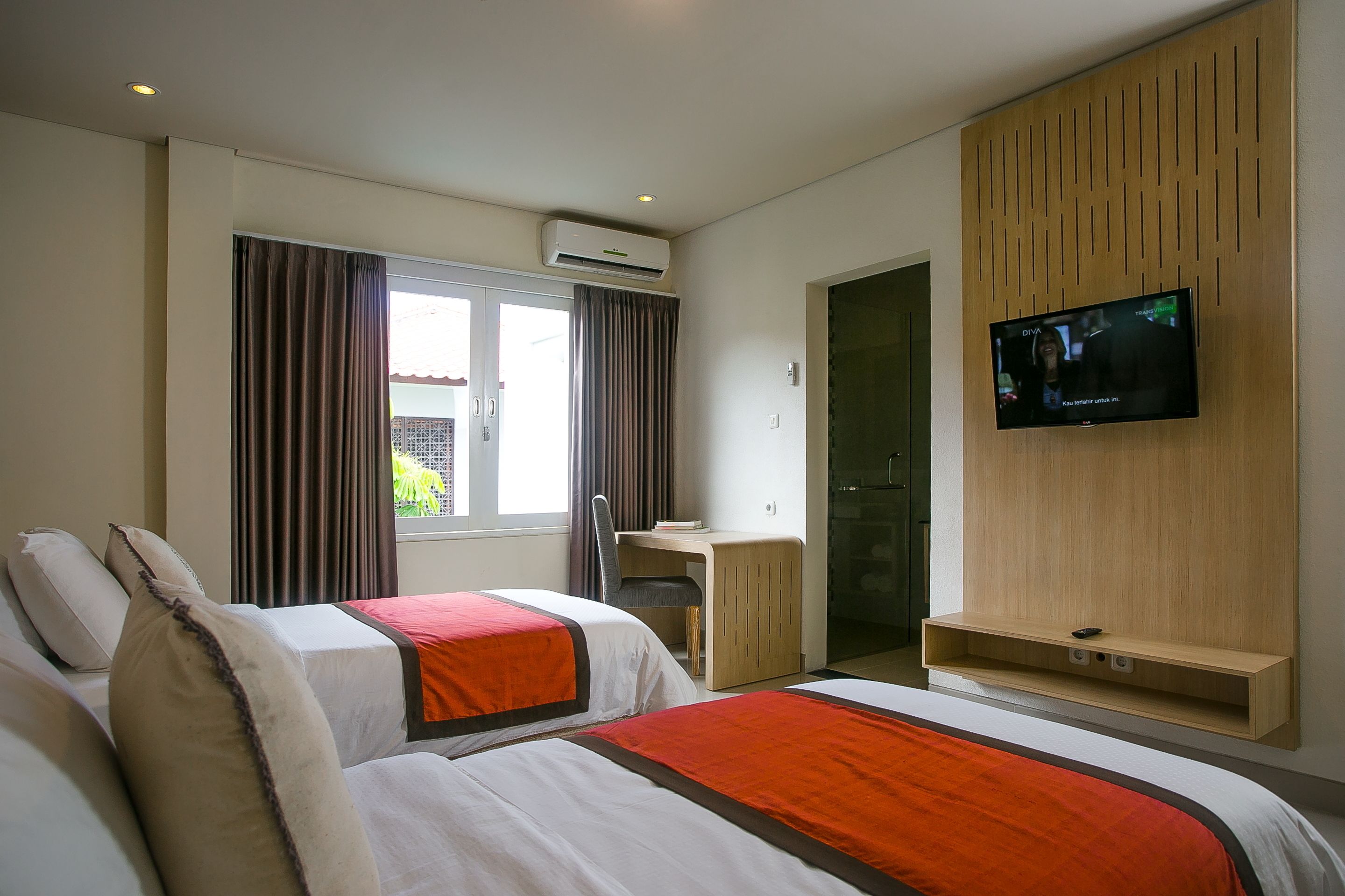 A hotel room with two beds, a desk, a TV, and a window with curtains.
