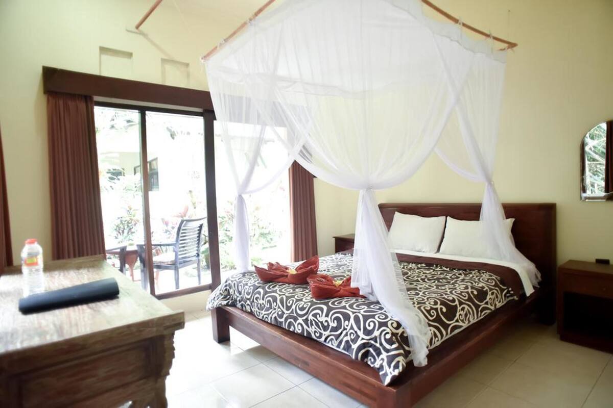 A bedroom with a four-poster bed, a wooden nightstand, and a table with a bottle.