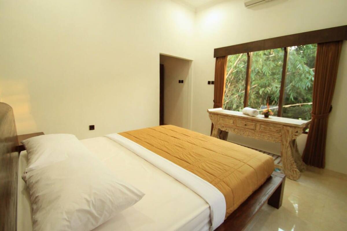 A bedroom with a bed, a wooden desk, and a window with curtains.