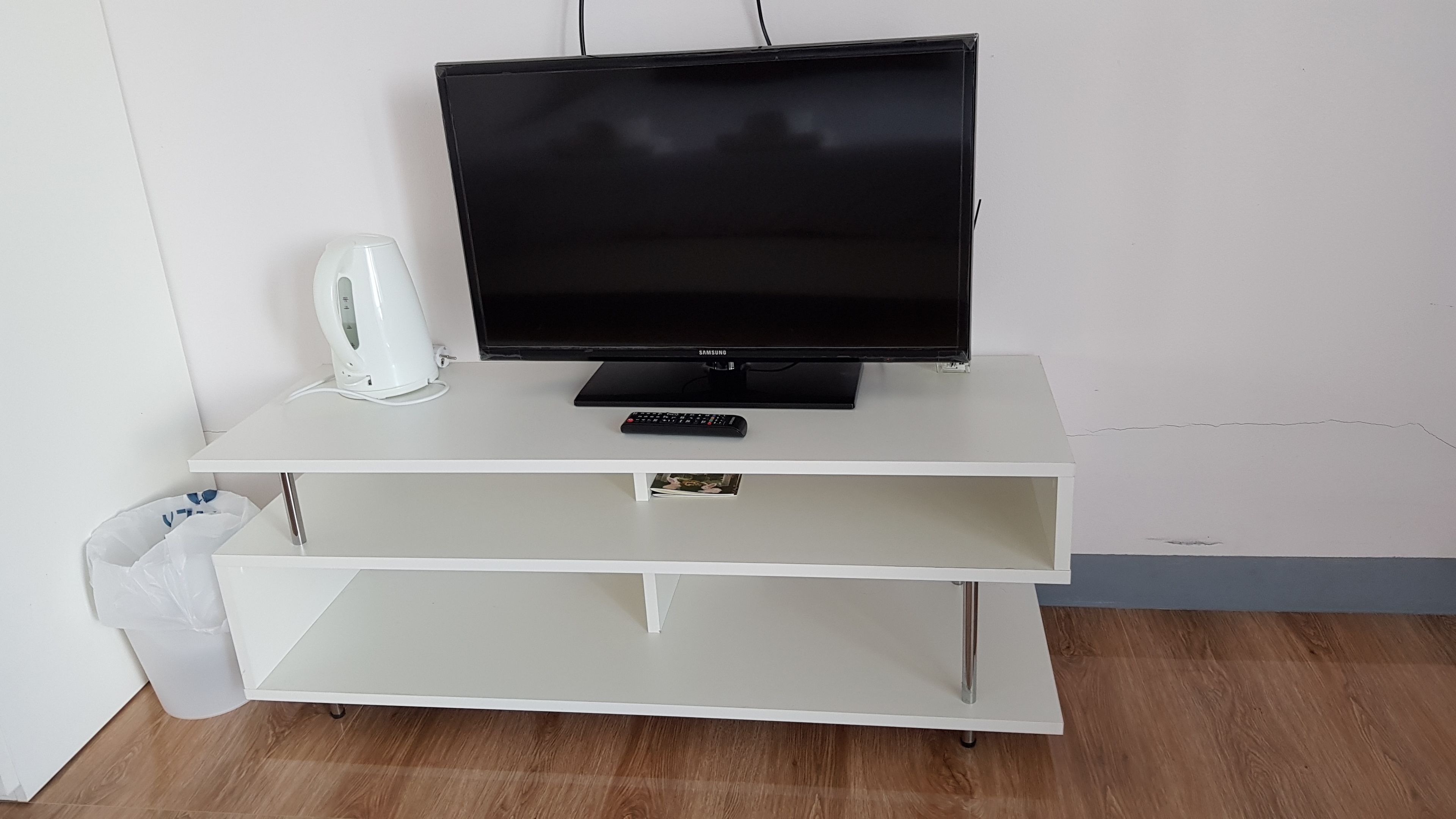 Un mueble bajo blanco para televisor con un televisor de pantalla plana, un control remoto y una tetera blanca.