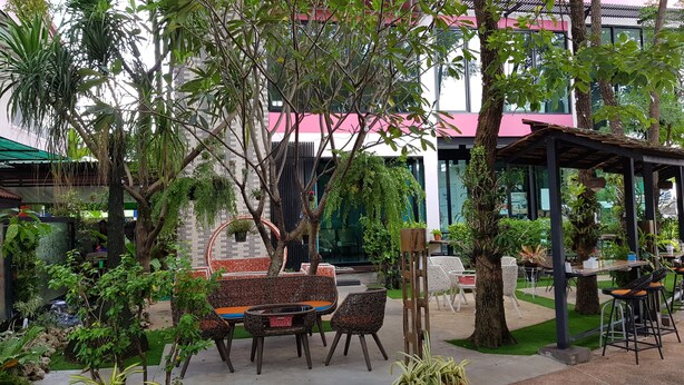 An outdoor seating area with wicker furniture, surrounded by lush greenery and trees. - Coffee Station Hostel (Udon Thani)