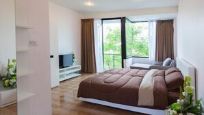A bedroom with a bed, a TV on a stand, and a balcony with curtains. - Coffee Station Hostel (Udon Thani)