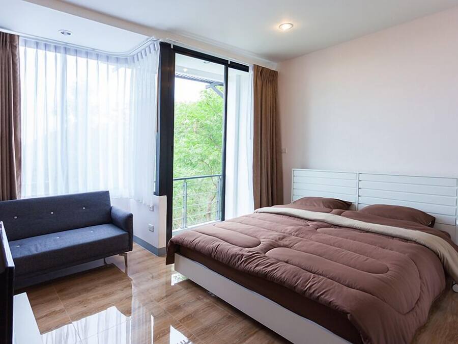 A modern bedroom with a large bed, a sofa, and a view of greenery outside.